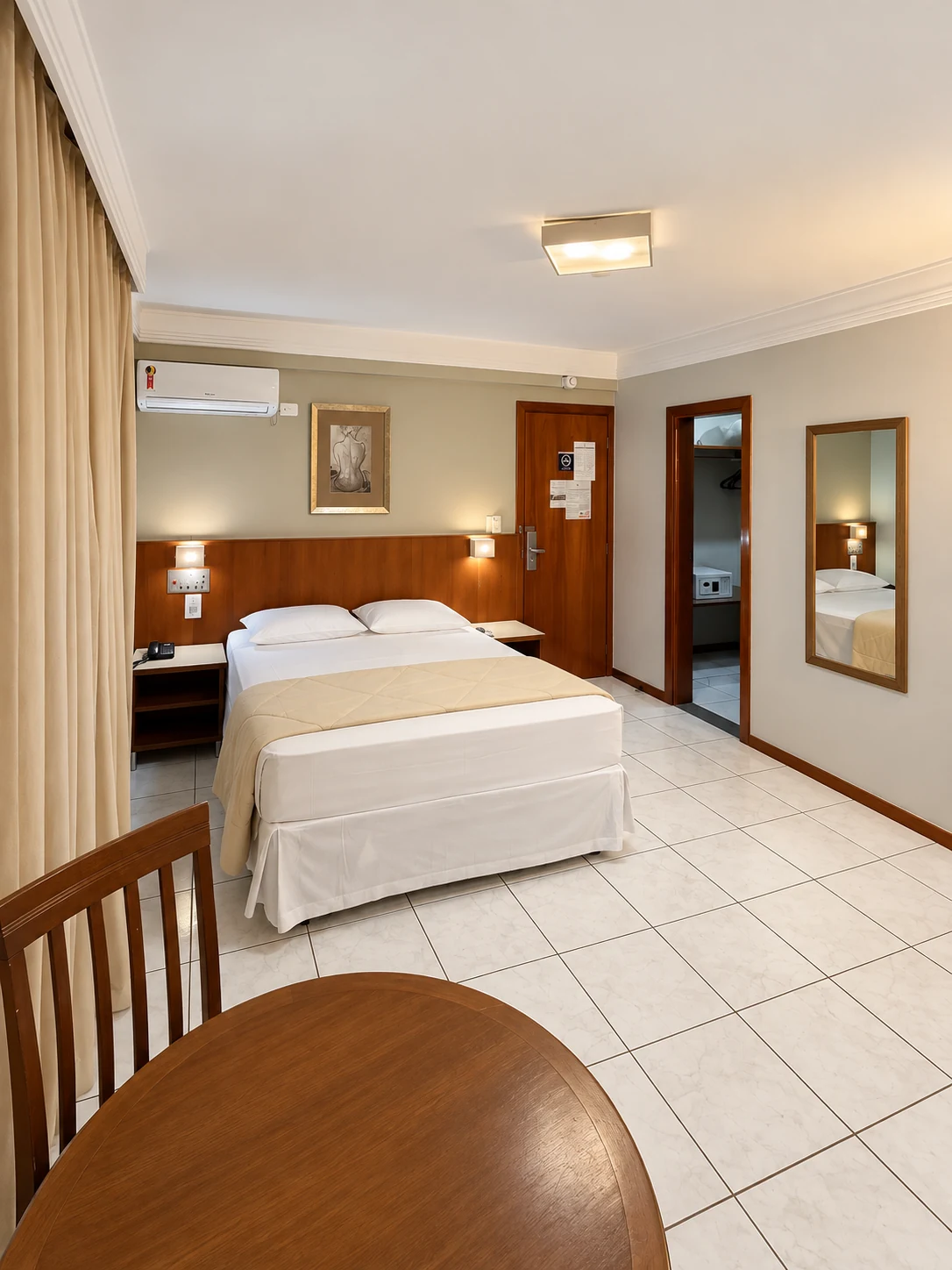 Quarto Luxo com cama de casal, mesa com cadeiras, espelho e ar-condicionado